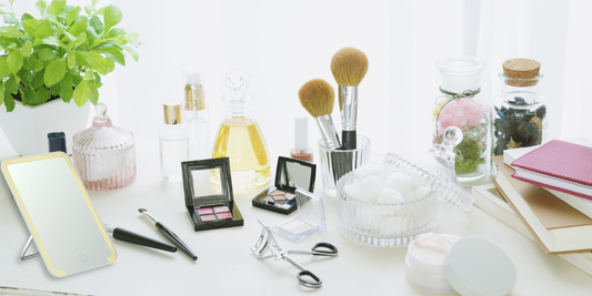 Makeup mirror with LED light on a modern vanity table surrounded by cosmetics, brushes, perfume bottles, and skincare essentials in a bright minimalist setting.